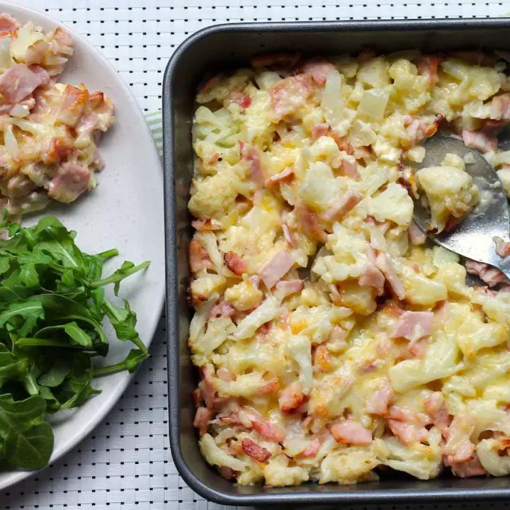 Keto Cauliflower Cheese Bake by Rachel Burke Aussie Keto Queen. Keto Cauliflower Cheese Bake is a must have in any keto repertoire The perfect keto side dish - loaded full of healthy fats and flavour! Keto Cauliflower Cheese Bake on a tray with green leafy vegetable on the side.