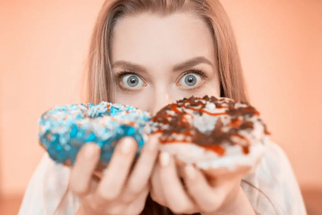 10 Tips for Cravings on the Ketogenic Diet: Why You Get Them & How to Stop. Why are cravings so hard to resist on Keto? Image of a beautiful woman holding 2 pieces of donuts.